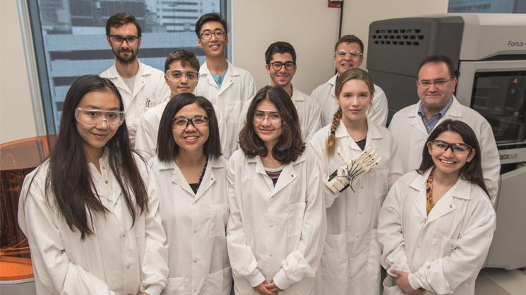 Front row from left to right are:  Ivy He, Ms. Tairong Zheng, Lauren Howe, Kaia Luik (holding a 3-D printed prosthetic hand), and Marjan Majid. Back row from left to right are:  Postdoctoral Fellow Luis Diaz-Gomez, Petros Zombanakis, Joe Li, Sebastian Chenin, Associate Director Anthony Melchiorri, and Professor Antonios Mikos.